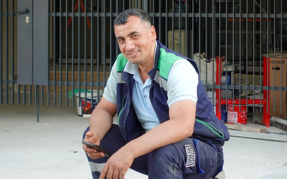 A worker in navy and green workwear holding a mobile phone outside a work site.